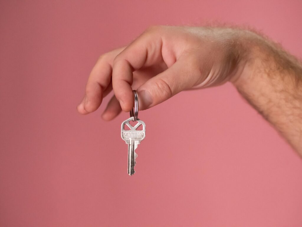 Hand holding a silver key with a pink background, symbolizing new home ownership.